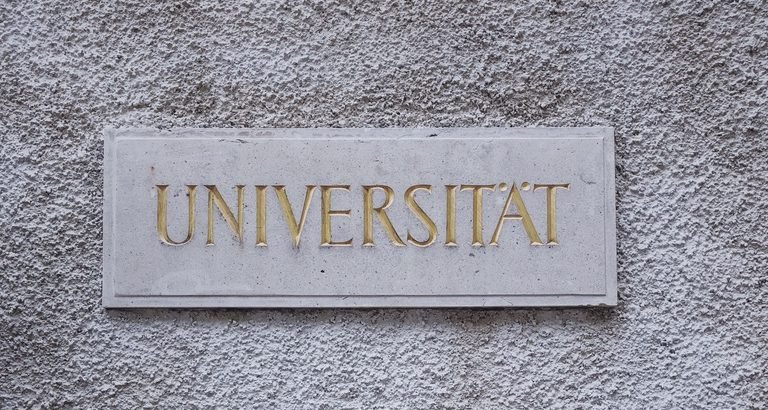 Gilded carved sign reading “Universität” on a rough stone wall